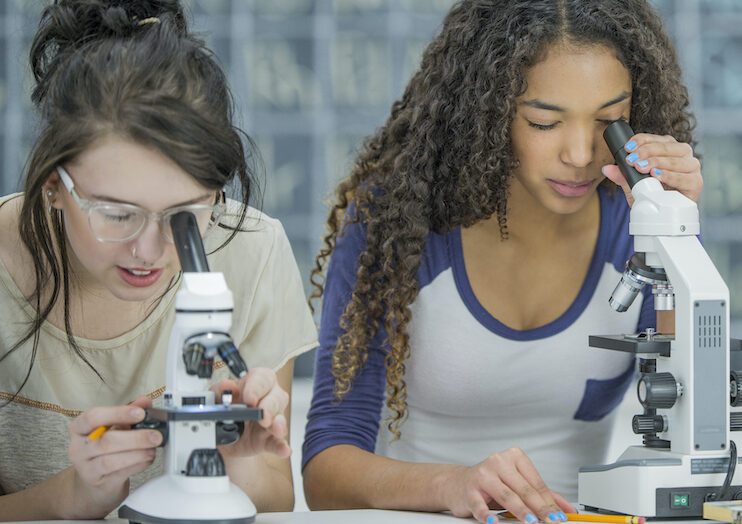 Viewing Slides Through a Microscope A multi-ethnic group of high school students are working in a science class together. They are looking at slides in biology class through a microscope.