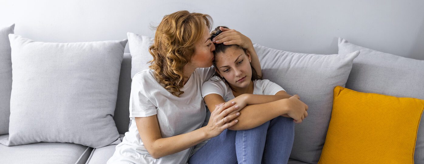 Caring mother calming and hugging upset little daughter Mother Talking With Unhappy Teenage Daughter On Sofa